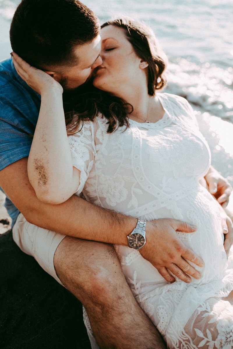 Seattle Maternity Photography, expecting mother sits back into her husbands embrace at the beach