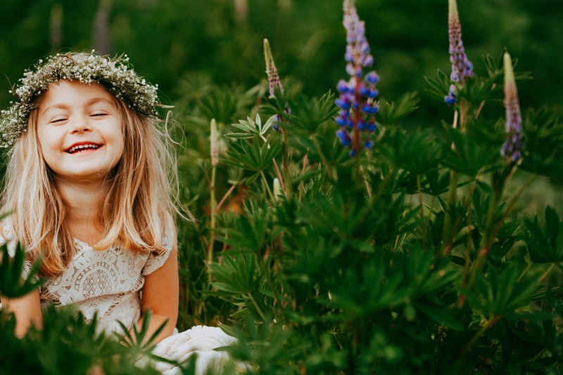 Seattle Motherhood Photography, a young girl laughs and smiles, she has a floral crown and sits near wild lavender outdoors
