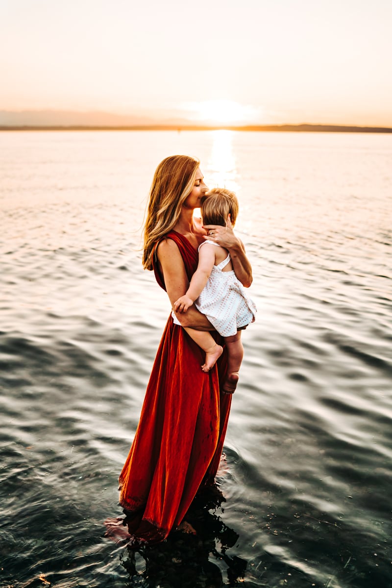 Seattle Motherhood Photography, A mother lovingly holds her baby daughter close to her as she stands in the quiet ocean waves