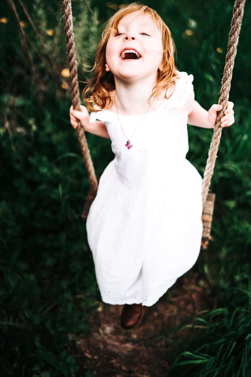 Seattle Motherhood Photography, a young girl swings excitedly on a tree swing near tall dark green grass