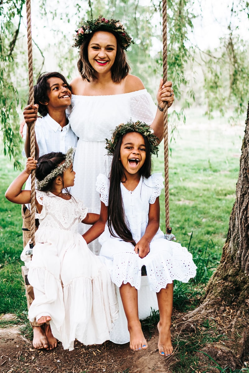 Seattle Motherhood Photography, Mom, son and two daughters huddle close all dressed in white, the girls wear floral crowns as they sit on a tree swing