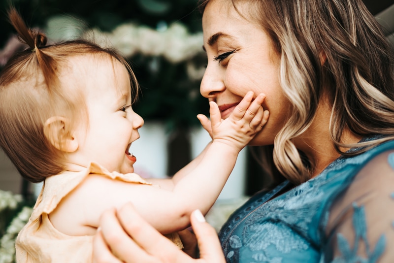 Seattle Motherhood Photography, a baby girl laughs and touches her mother's cheek as mom happily gazes right back at her