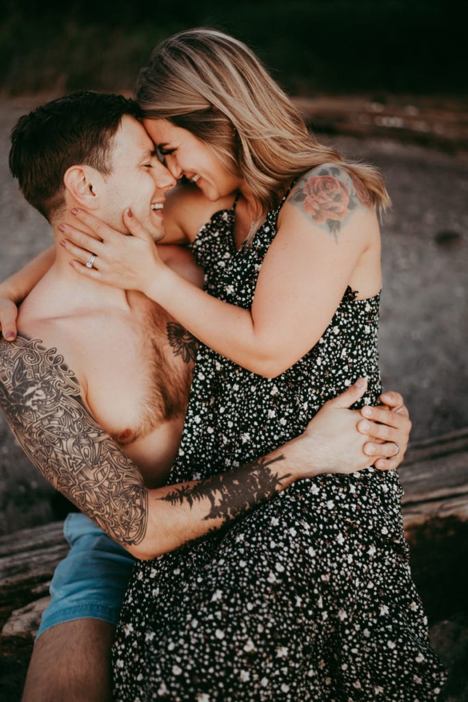 Family Photographer, A man with tattoos on his arm holds a woman on his lap, they smile face to face