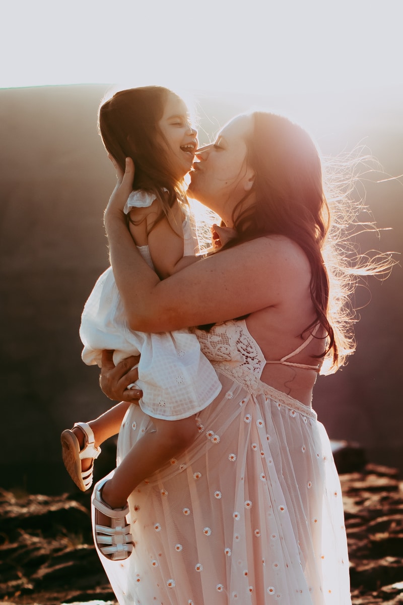 Seattle Maternity Photography, a mother holds her toddler girl and kisses her on the chin, mom is expecting