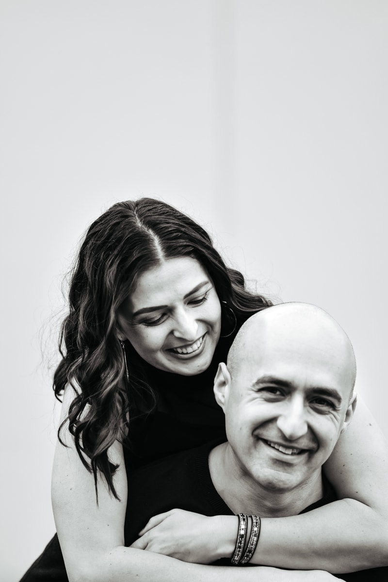 Seattle Couples Photography, woman wraps her arms loving around her husband from behind, they both smile