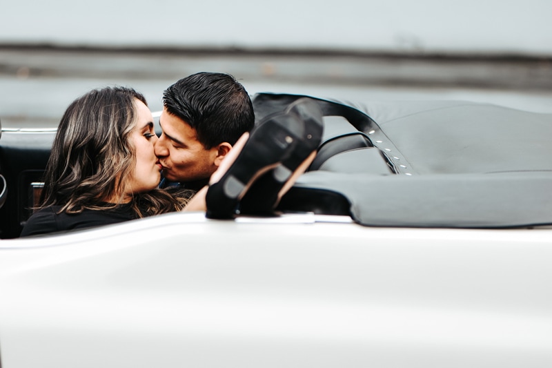 Seattle Couples Photography, two people in love kiss inside a convertible, the woman's fee hang up out and above the door as she reclines into him