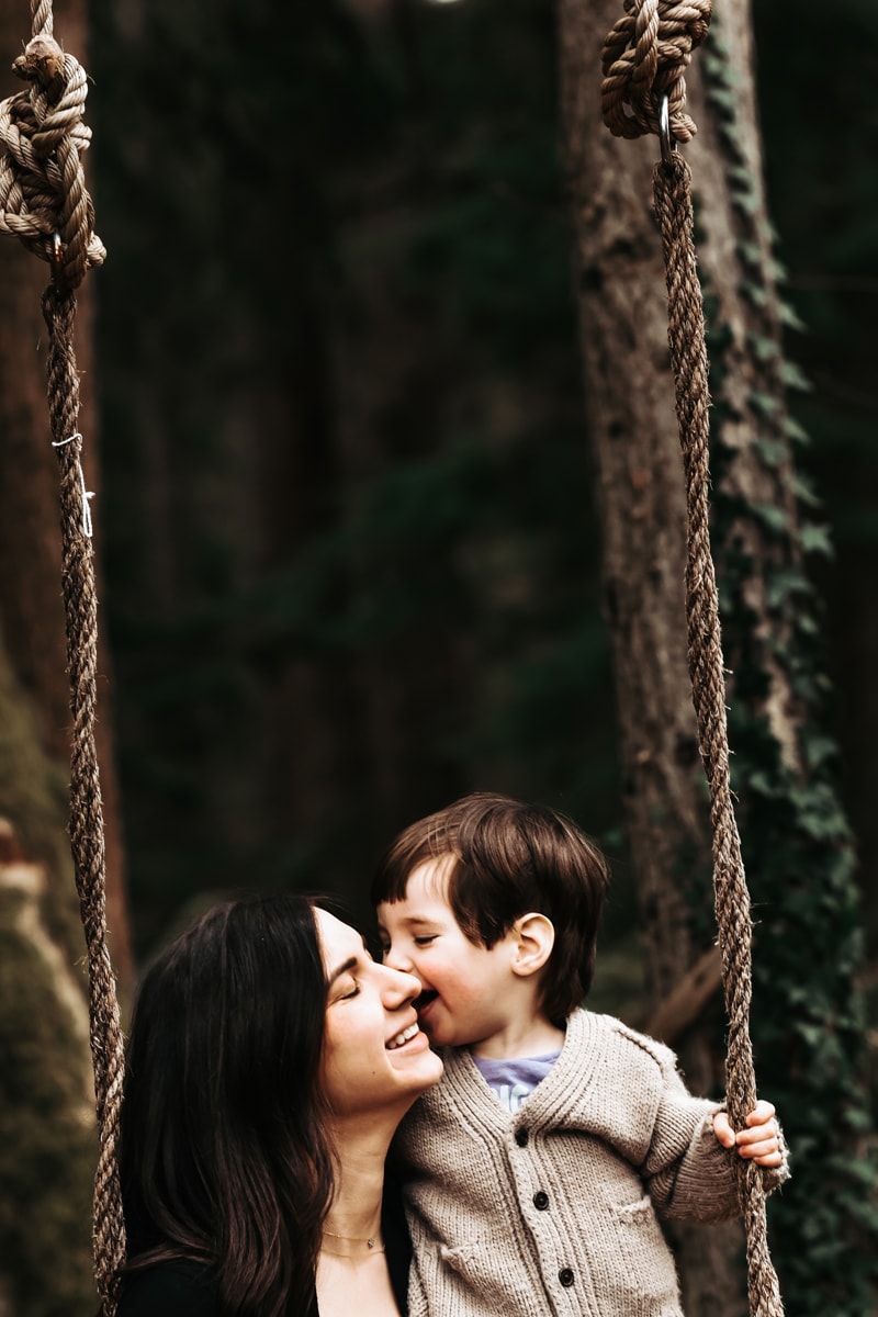 Seattle Motherhood Photography, a little boy in a cardigan leans into his mother on a tree swing in the forest