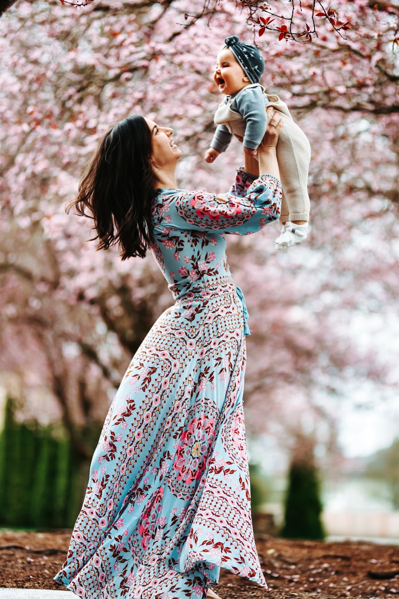 Seattle Motherhood Photography, a mother holds her baby daughter in the air beneath a cherry blossom tree.