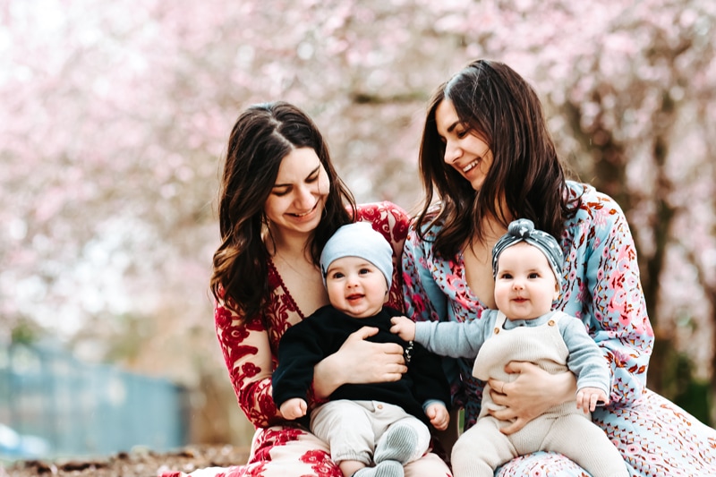 Seattle Motherhood Photography, two moms hold their two babies, everyone smiles under a large cherry blossom tree