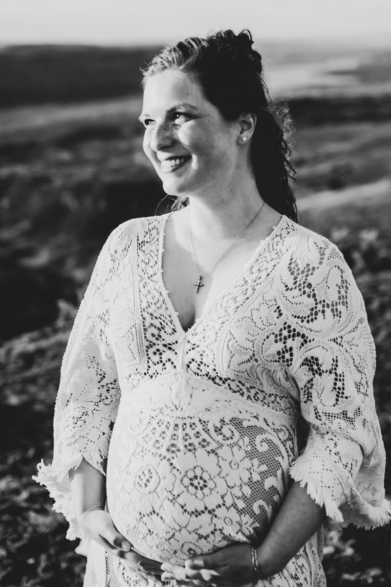 Seattle Maternity Photography,  a woman smiles and holds her belly as to feel her baby kick, she is outdoors