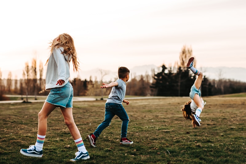 Seattle Motherhood Photography, kids play in the grass, a girl does a cartwheel and a boy runs toward her