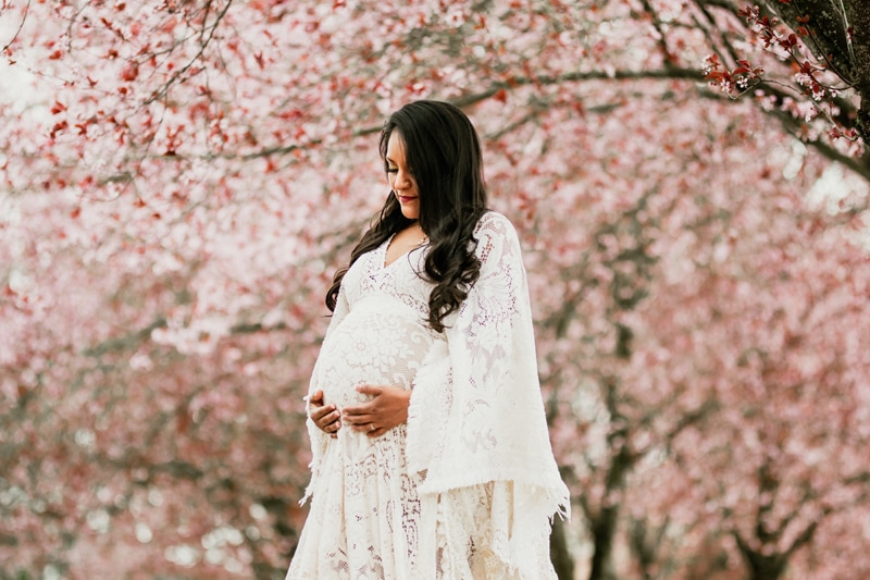 Seattle Maternity Photography, a pregnant woman in a white lacy dress walks under cherry blossom tree
