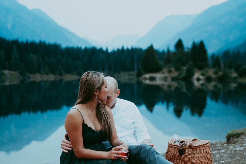 Seattle Couples Photography, a man and woman are having a picnic near a lake in the forest, he kisses her shoulders