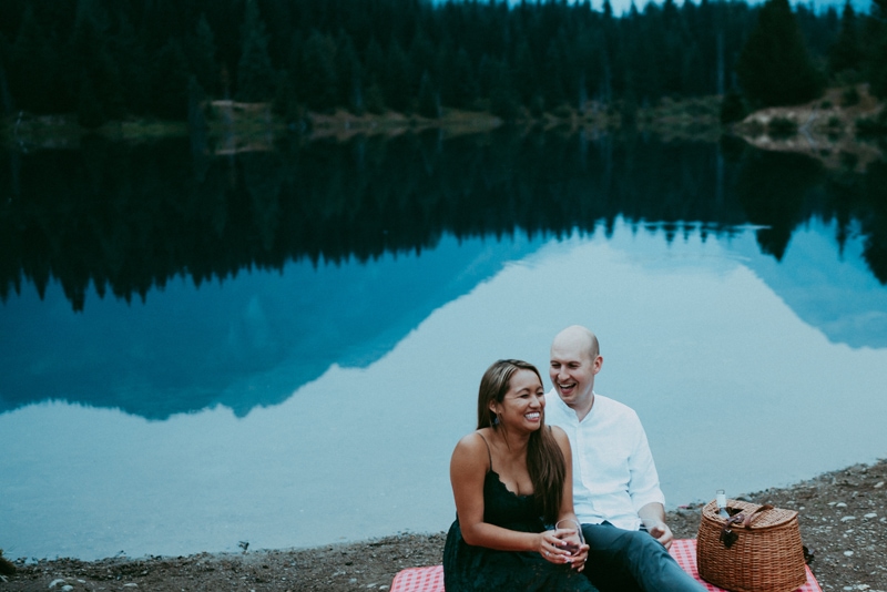 Seattle Couples Photography, a husband and wife laugh together on a picnic blanket near a lake